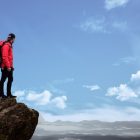 Hiker in red jacket stands on a cliff edge, overlooking a scenic mountain view under a bright blue sky.